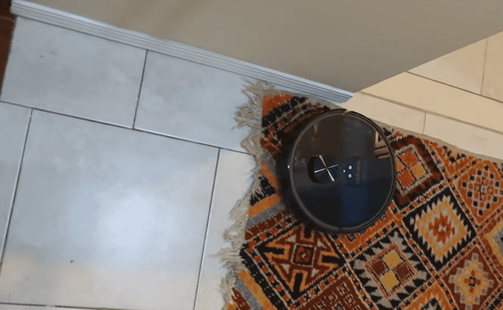 Un robot aspirateur sur un tapis à côté d'un sol carrelé.
