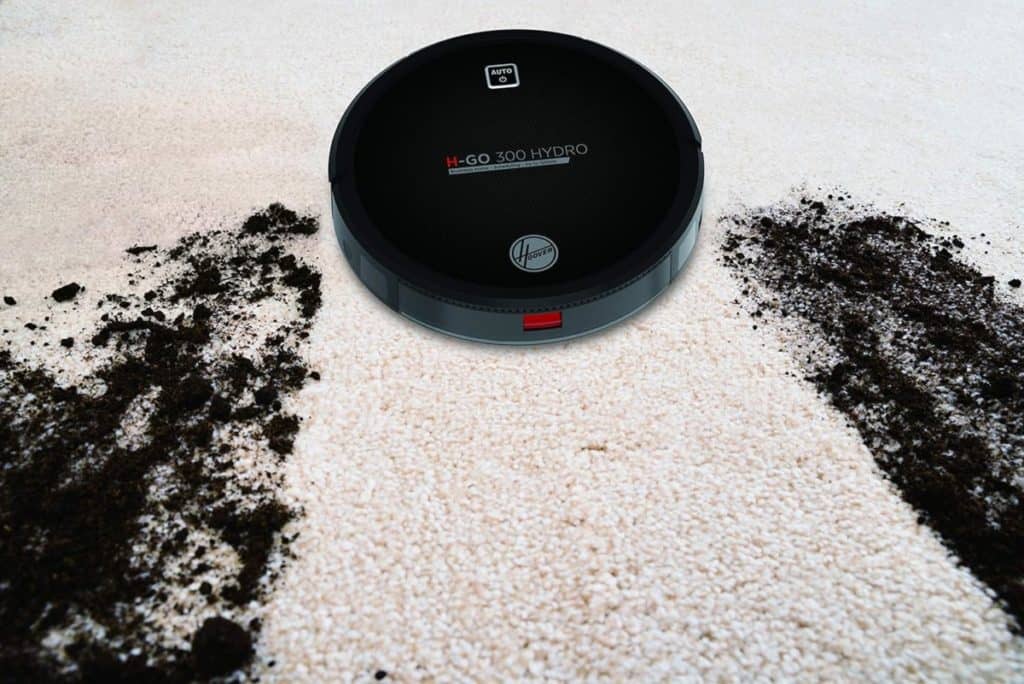 Un aspirateur robot naviguant sur un tapis blanc parsemé de taches sombres.